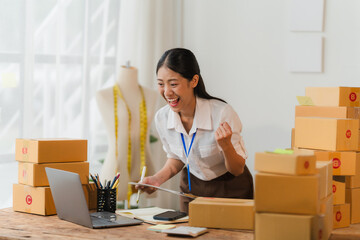 Small Business Success: A triumphant female entrepreneur celebrates a milestone in her e-commerce business, surrounded by stacks of packages and a laptop.