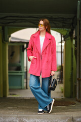 A woman in a bright pink coat and sunglasses waiting for taxi in a colorful urban setting
