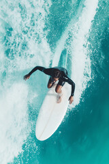 Top view of woman surfing on a bright blue ocean during a sunny day with strong waves and clear skies overhead 