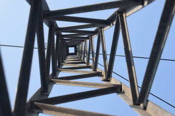Steel structure of a high voltage pylon with wires, insulators blue sky and sun seen from...