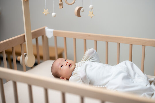 Newborn baby with swaddle and lying on the baby cot with look at the toy