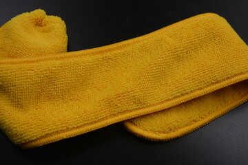 An unusual cleaning cloth, a long yellow microfiber set on a black, matte plastic background.