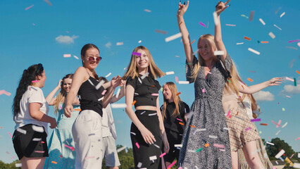 High school graduates joyfully tossing colorful confetti under a clear blue sky