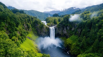 Fototapeta premium Majestic waterfall cascading down a lush green mountainside into a serene pool, surrounded by dense forest and mist.