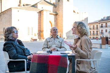 three middle aaged friends chatting and enjoying outdoor time at a cafe near a historical landmark