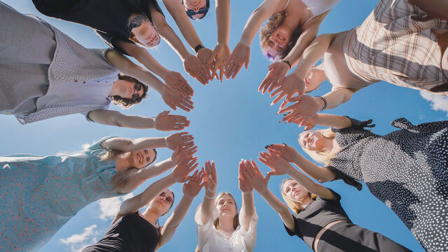 High school students joining hands in a circle under the clear blue sky, showcasing unity, teamwork, and collaboration