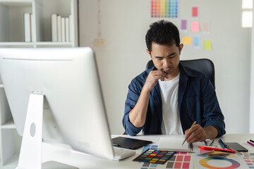 Naklejka premium Young Male Graphic Designer Focused on Creative Project at Modern Workspace with Computer and Color Swatches