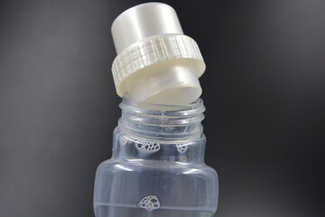 A large transparent plastic bottle with a matte pink liquid and a golden-pearlescent round cap is located on a black plastic background. Liquid for cleaning, washing in the bathroom, laundry room.