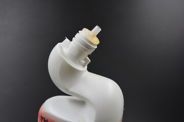 A white plastic bottle with a curved neck and a yellow cap is placed on a black plastic background....