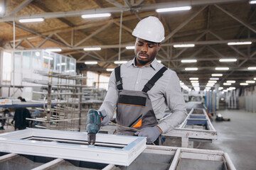 Factory worker assembling pvc window frame using electric screwdriver