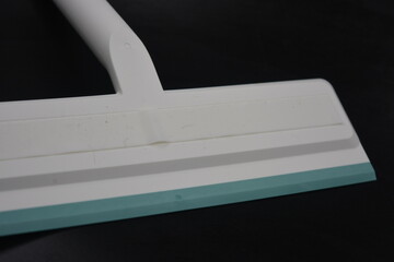 Plastic white tool, an object with a green elastic band for washing and cleaning windows located on a black, matte plastic background.