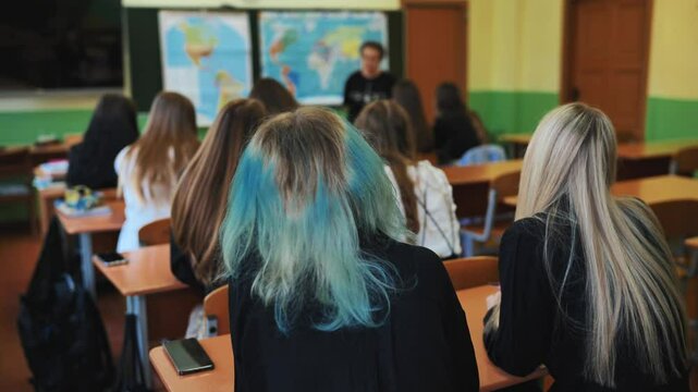 Teenage students are engaged in a geography lesson in the classroom, paying close attention to their teacher and the world map
