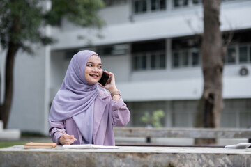Fototapeta premium Confident Muslim Girl Student in Hijab Using Smartphone and Studying Outdoors at University Campus