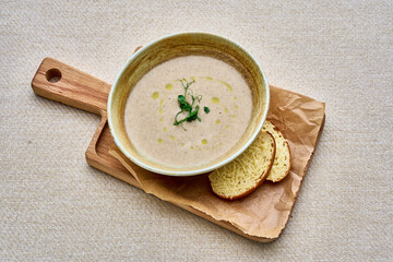 A bowl of soup with a piece of bread on a wooden cutting board