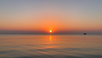 Obraz premium Serene Sunset Over Calm Ocean With Distant Vessel