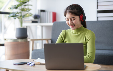 Fototapeta premium Asian woman focused on work with headphones and laptop in modern office, concept of concentration