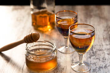 Still life close-up of two glasses of honey mead (medovukha) with honey dipper on wooden surface, dramatic side light