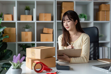 Young Female Entrepreneur Managing Online Sales in a Home Office Surrounded by Shipping Boxes and Supplies