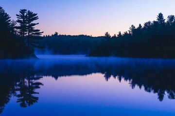 A peaceful lake at dusk with mist rising, reflecting the silhouettes of trees against a calming twilight sky.