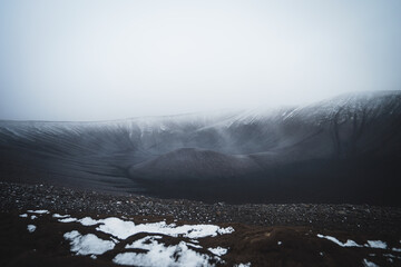 The edge of the Hverfjall volcanowith the black tuff ring in snowy and misty weather