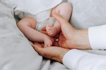 A baby is being held by two people, one of whom is wearing a wedding ring. The baby is on a bed, and the people are holding it close to their chest. Concept of warmth and love