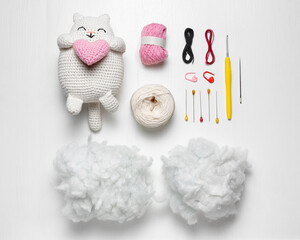 A crochet kit with a finished cat holding a heart, yarn, stuffing, crochet hooks, needles, pins,...