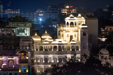 Fototapeta premium Aerial drone shot of brightly lit building exterior with elegant arches, ornate balconies and roof with guests enjoying the evening in Udaipur