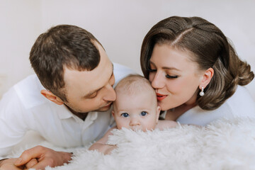 A man and a woman are kissing a baby. The baby is looking at the camera. Scene is loving and tender