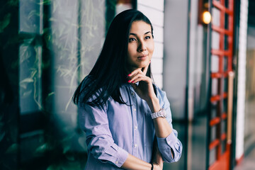Obraz premium Charming positive pensive brunette woman dressed in stylish clothes dreaming about successful business startup indoors.Gorgeous contemplative hipster girl pondering while standing in modern office