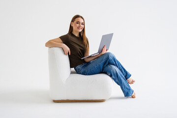 Beautiful woman is sitting on couch and is looking laptop on white background.