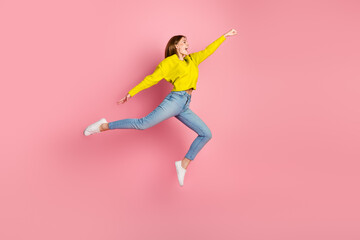 Happy young red-haired woman leaping against pink background, expressing joy and excitement,...