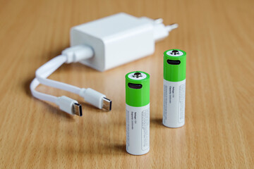 Rechargeable batteries with power adapter and USB lead on wooden surface, close-up, on wooden surface