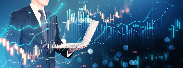 Businessman holding a laptop with financial charts and data visualizations on a digital blue background.
