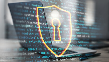 Digital shield with keyhole overlay on programming code and laptop screen, symbolizing cybersecurity and data protection.
