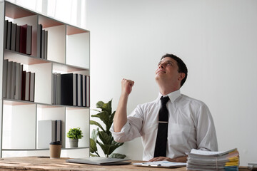 Young Businessman Celebrating Success in Modern Office with Joyful Expression and Raised Fist