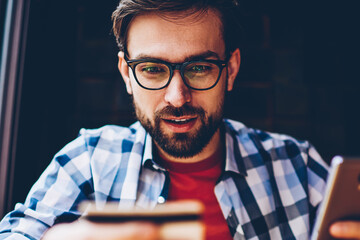 Wondering bearded young man in optical eyeglasses looking at number of business card to calling on...