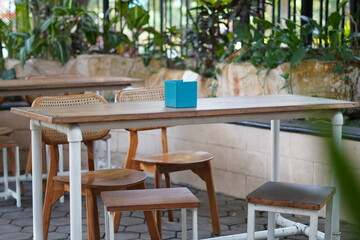 A minimalist wooden table and chairs in a cafe with a blue tissue holder in the middle without...