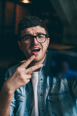 Excited male blogger showing peace fingers and taking funny pictures on mobile camera indoors, young emotional hipster guy making photos for social networks connected to wifi on smartphone device