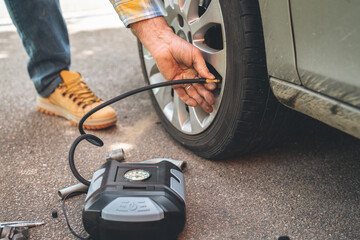 Man using a portable air pump to inflate car tire on a sunny day in a parking area