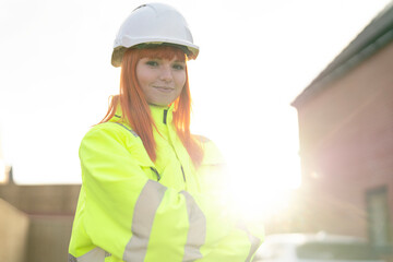 Brightly dressed young pretty female worker stands confidently at sunset near construction site