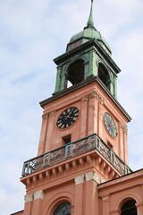 close-up of a pink church tower with large clock and bells