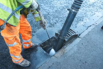 Worker cleans storm drain to remove debris and improve water flow in urban area during daytime...