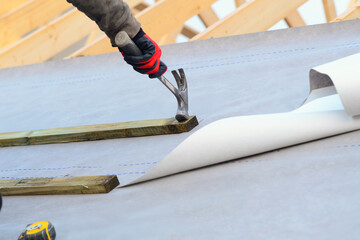Roofer installing roofing waterproof membrane underlayment using nails and tools on a construction...