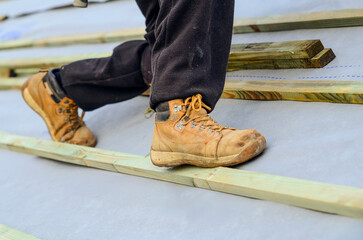 Construction worker roofer walking on wooden beams while wearing safety boots at a building site...