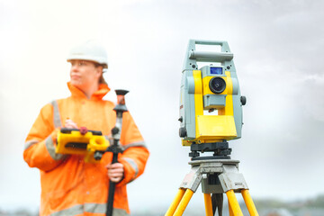 Female Surveyor conducting land measurements with advanced equipment under overcast sky in urban environment