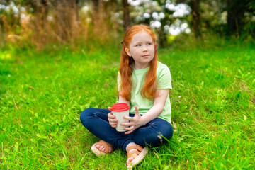 Fototapeta premium Young girl enjoying a warm drink while sitting on grass in a serene outdoor setting