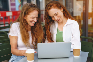 Two women enjoying coffee and working together on a laptop at an outdoor cafe in the afternoon