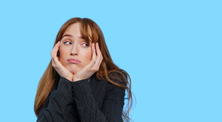 Woman displaying boredom with her chin resting on her hands against a blue background in a studio setting