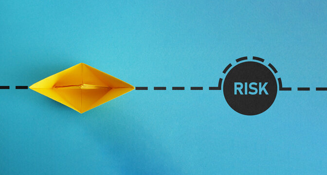 Overcoming challenges and navigating uncertainty. Paper boat sailing around the word risk.