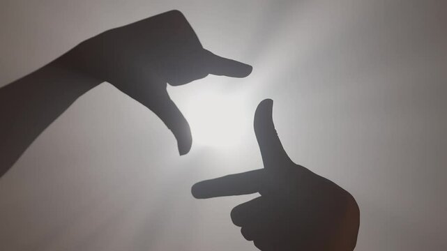 Hand silhouette, person showing gesture making photo frame fingers sign against bright colored spotlight, isolated on studio background close up shot.